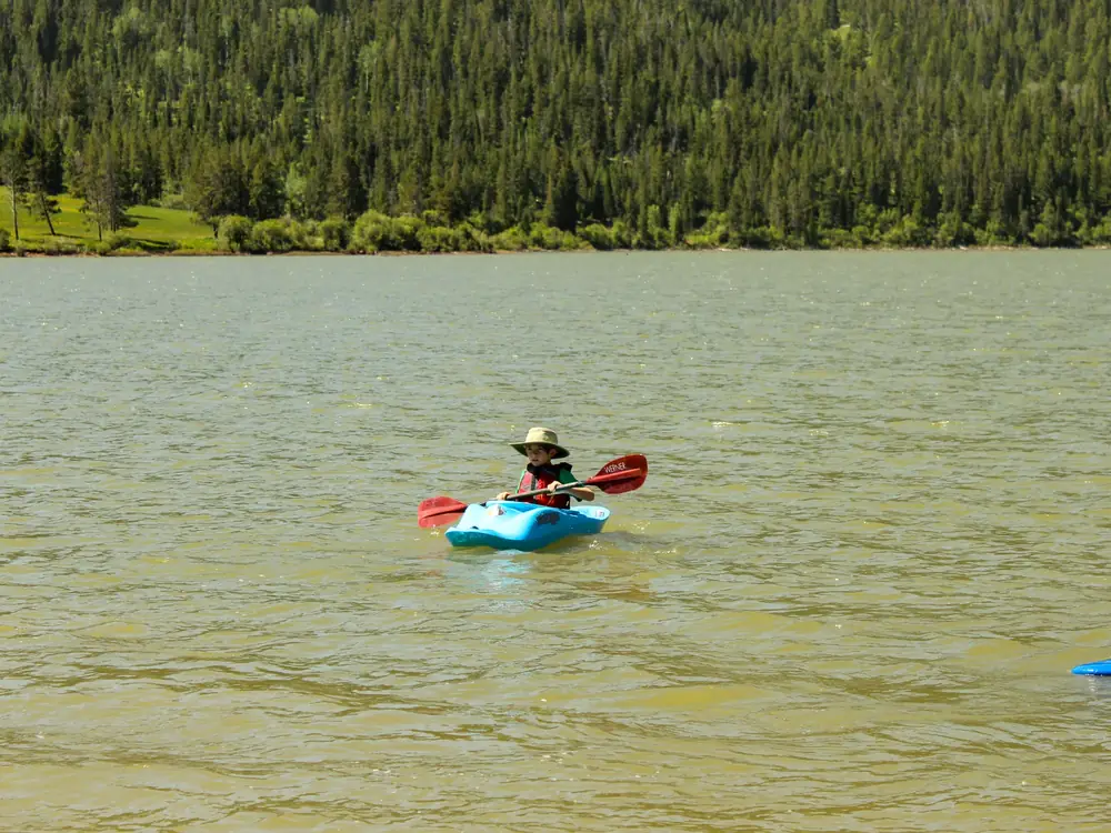 Single person in a small blue kayak on a lake and red double-bladed paddle in Slide Lake.