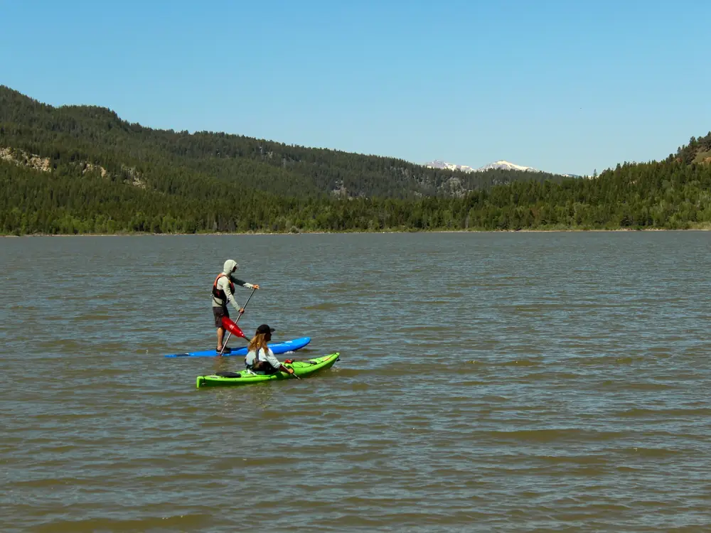 Two people on a body of water and one person standing on a blue paddleboard using a paddle with a red blade in Jackson Hole