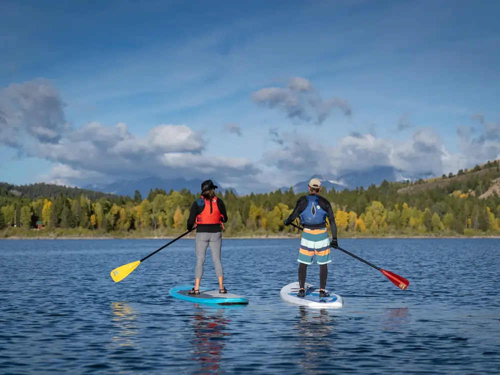 Two people standing on stand-up paddleboards and each person holding a paddle in Jackson Hole.