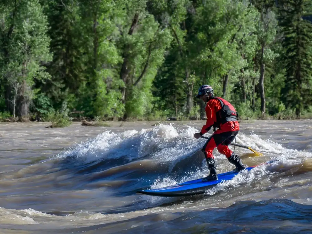 One person standing on a blue board and yellow paddle in the person’s hands in Jackson Hole.