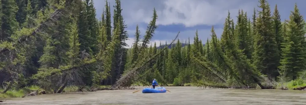 One person in blue inflatable raft on river in Yellowstone National Park.