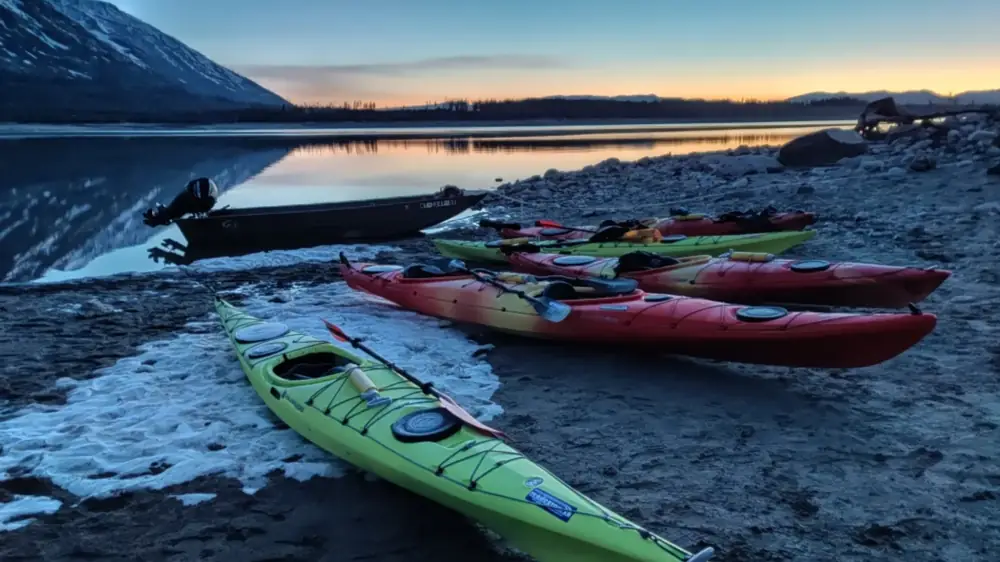 Six kayaks on rocky shoreline and two green kayaks in foreground in Yellowstone National Park.
