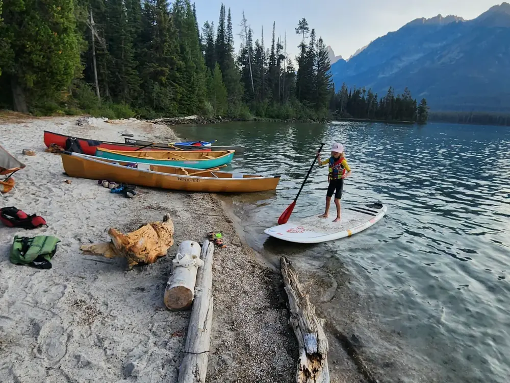 One person standing on a white stand-up paddleboard near shore in Yellowstone National Park.