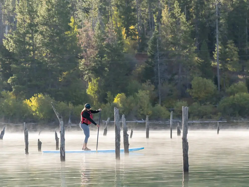 One person standing on a stand-up paddleboard and person holding a paddle in Slide Lake.