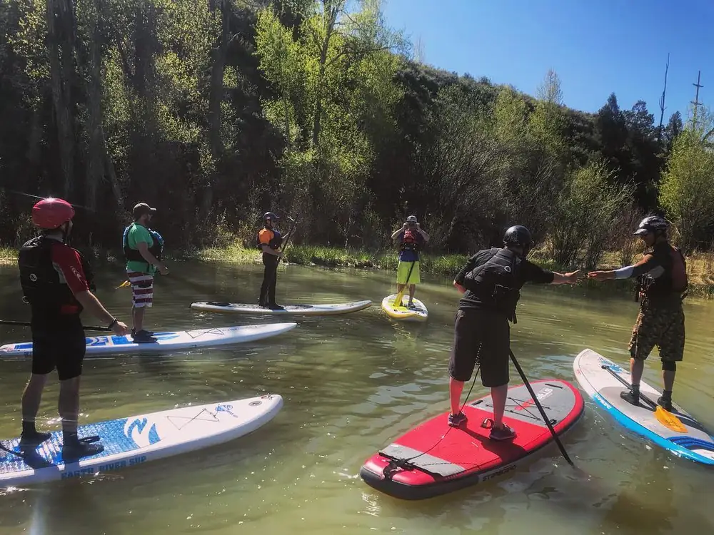 One person standing on a blue board and yellow paddle in the person’s hands in Jackson Hole.