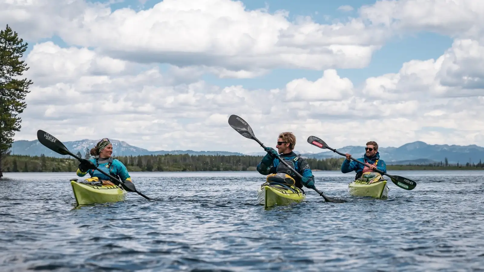 Three people in yellow kayaks and calm lake water in Yellowstone National Park.