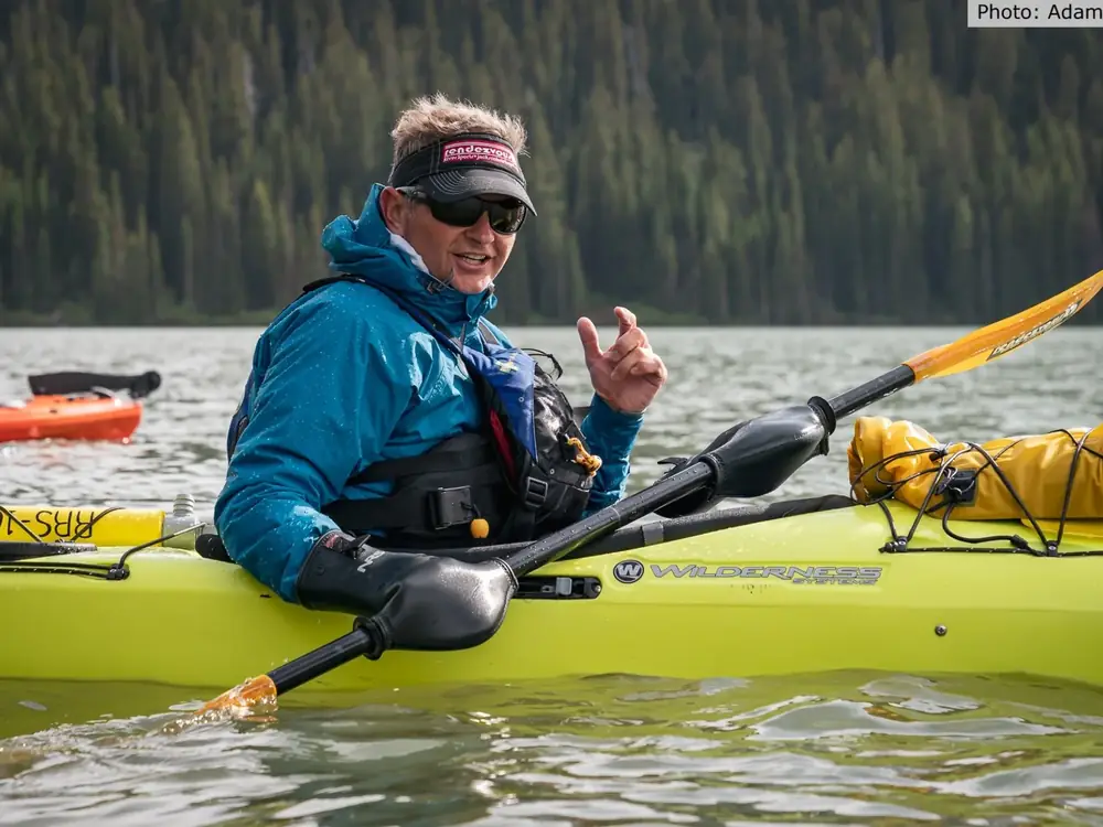 Person standing and gesturing and yellow kayak on grass in Yellowstone National Park.