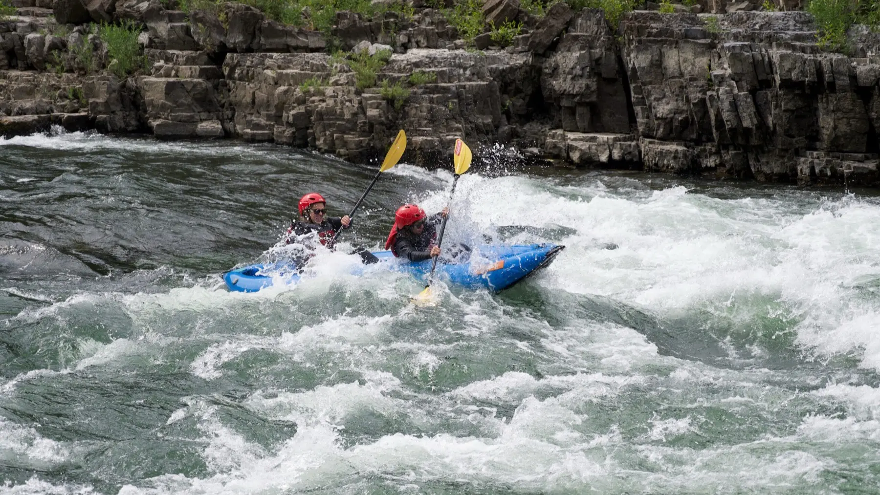 Two paddlers in a blue inflatable kayak navigating whitewater rapids